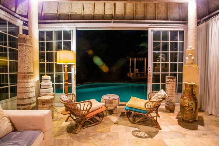The lit living room seen from across the pool at night