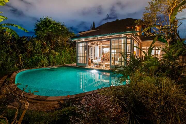 The villa lit from within at dusk, reflected in the pool